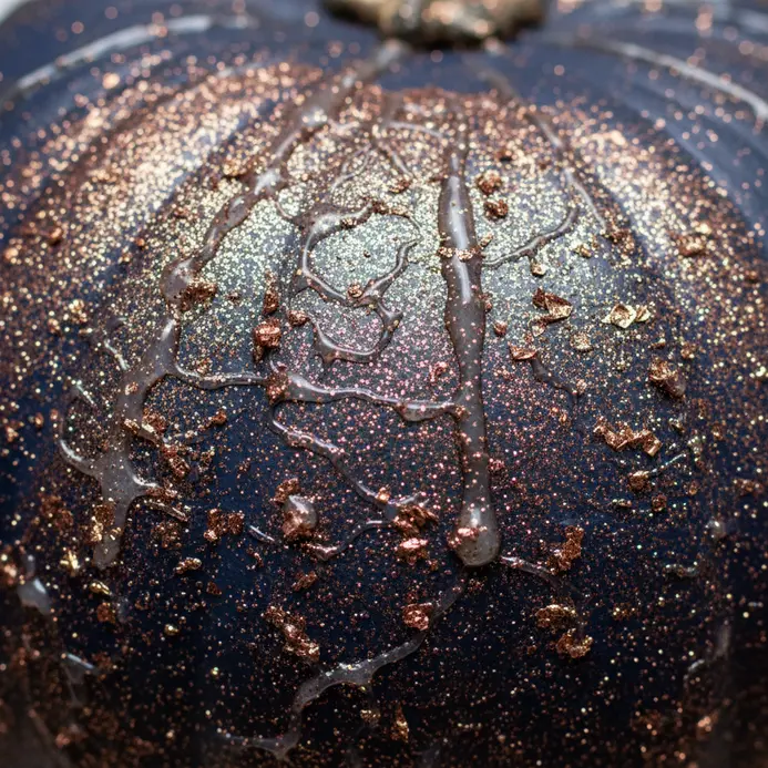 Gold glitter is sprinkled over a wet adhesive layer on a pumpkin's stem area.