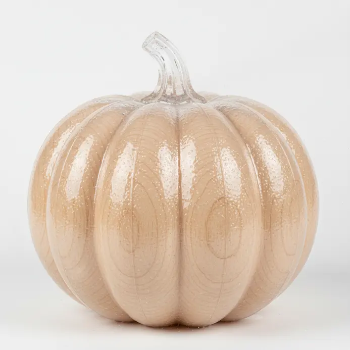 A hand sprays a clear matte sealant in a well-ventilated area over a decorated pumpkin.