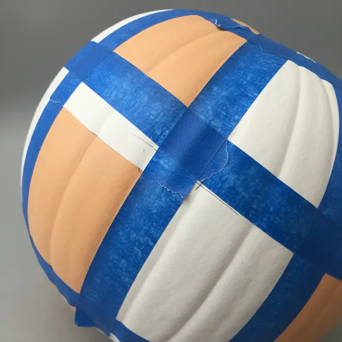 A pumpkin with strips of blue painter's tape forming sharp angles and lines.