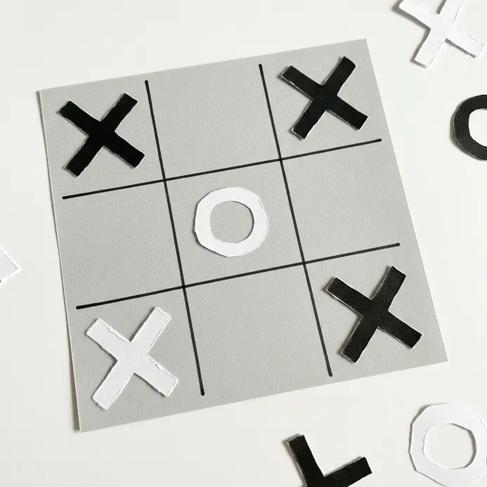 A flat cardstock tic tac toe board with X and O pieces cut from contrasting colored paper.
