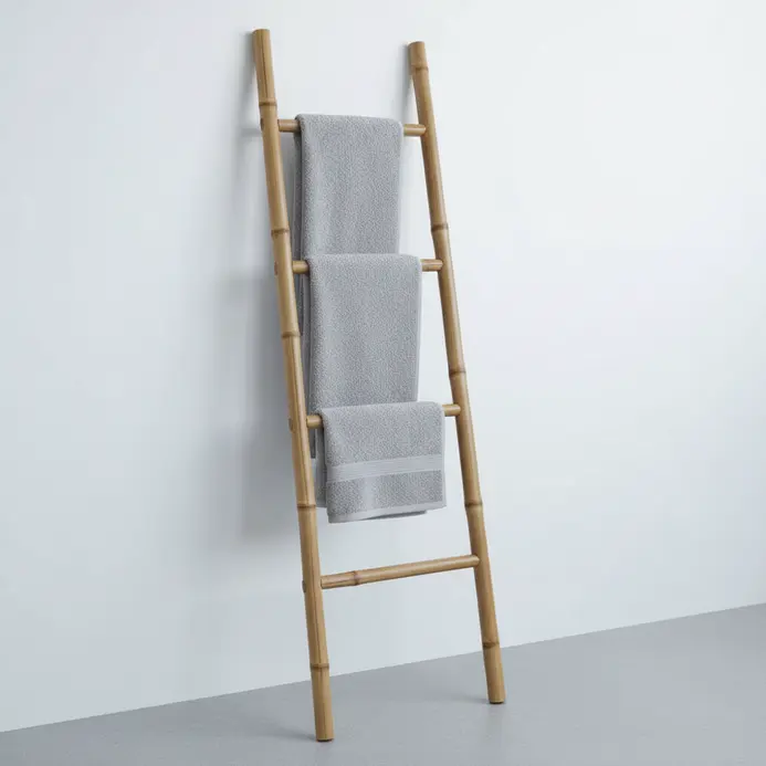 A small bamboo ladder leaning against a wall with towels draped over its rungs.