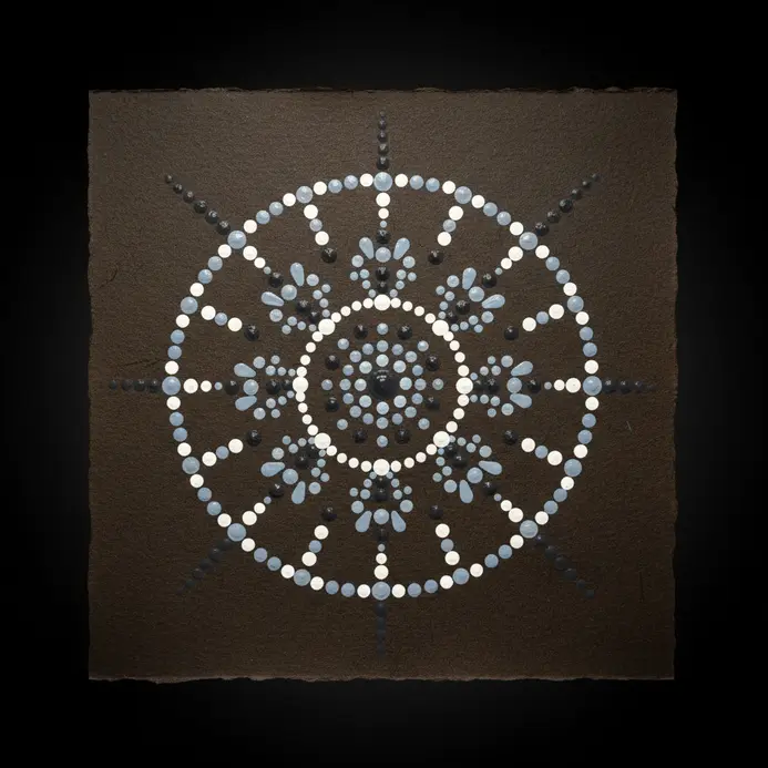 A polished black stone with a simple, elegant mandala pattern made of crisp white dots.