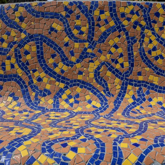 A colorful pattern made from small, hand-placed ceramic tiles on a concrete surface.