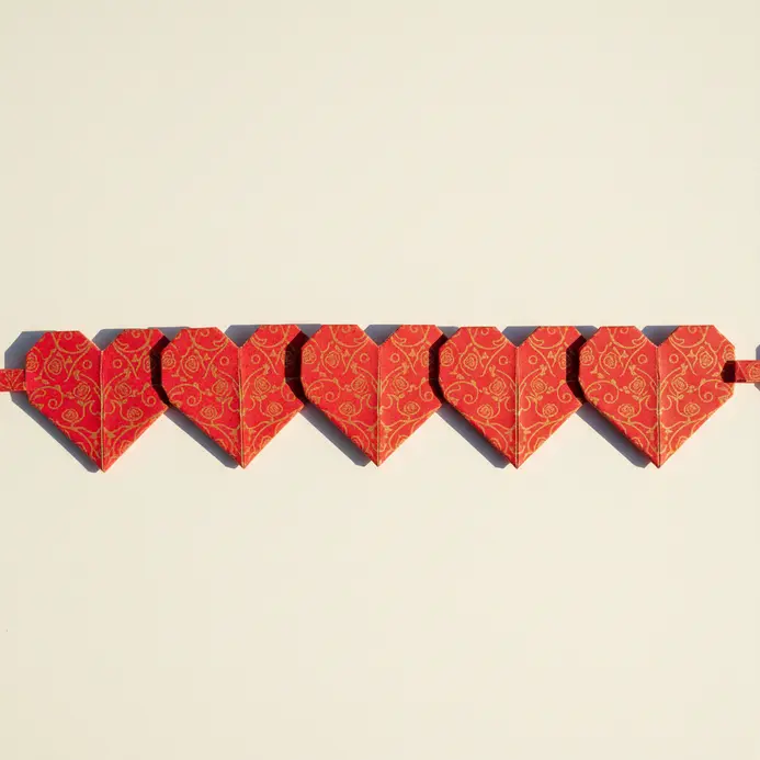 A decorative paper garland consisting of multiple folded origami hearts in patterned red paper, linked together.