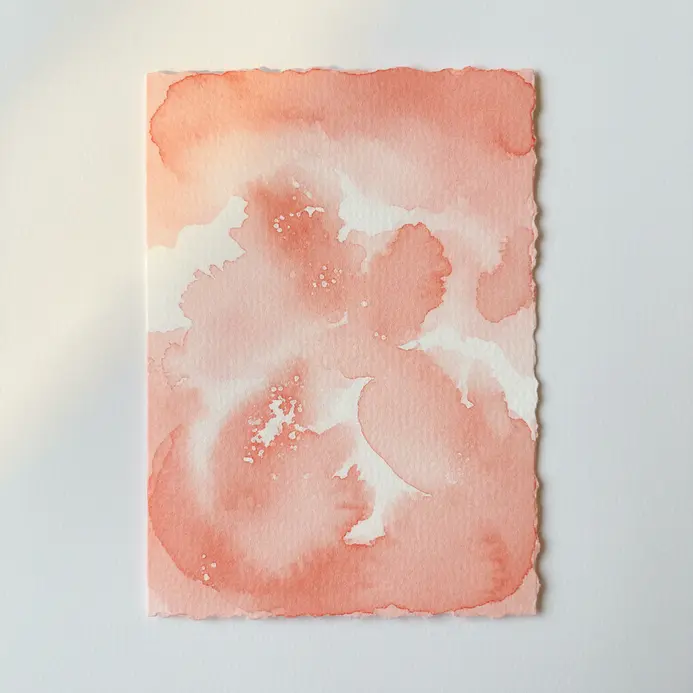 A handmade card featuring a crisp white heart design revealed through a watercolor resist technique on a pink background.