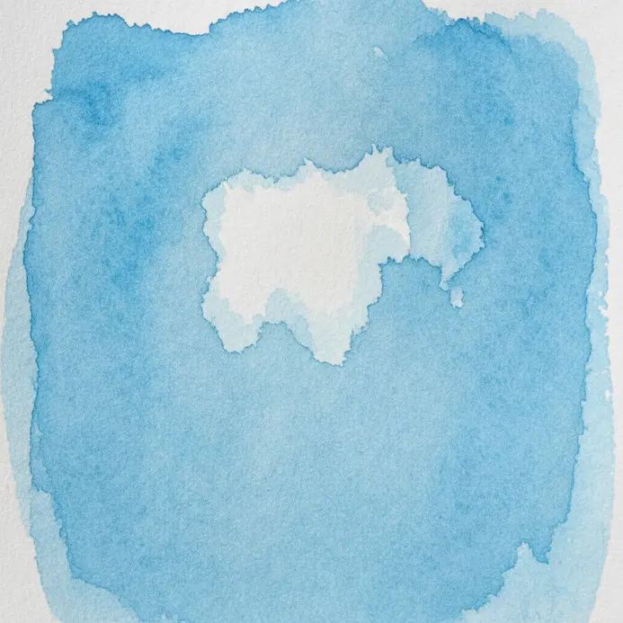 A clean, damp brush lifting a streak of blue paint from a still-damp wash on cold press paper.