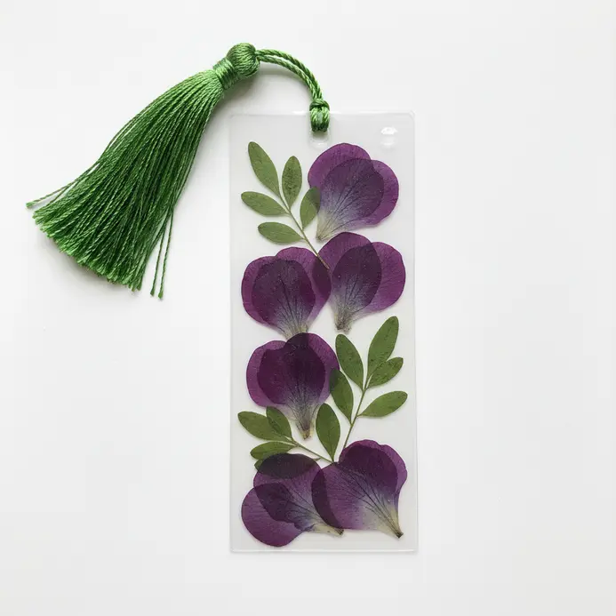 A clear, laminated bookmark with a pressed purple violet in one corner and a green silk tassel at the top.