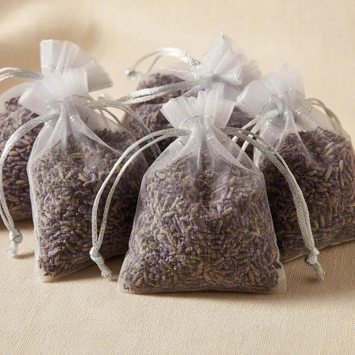 Three small drawstring sachets made from sheer white fabric, filled with dried purple lavender, resting on linen.