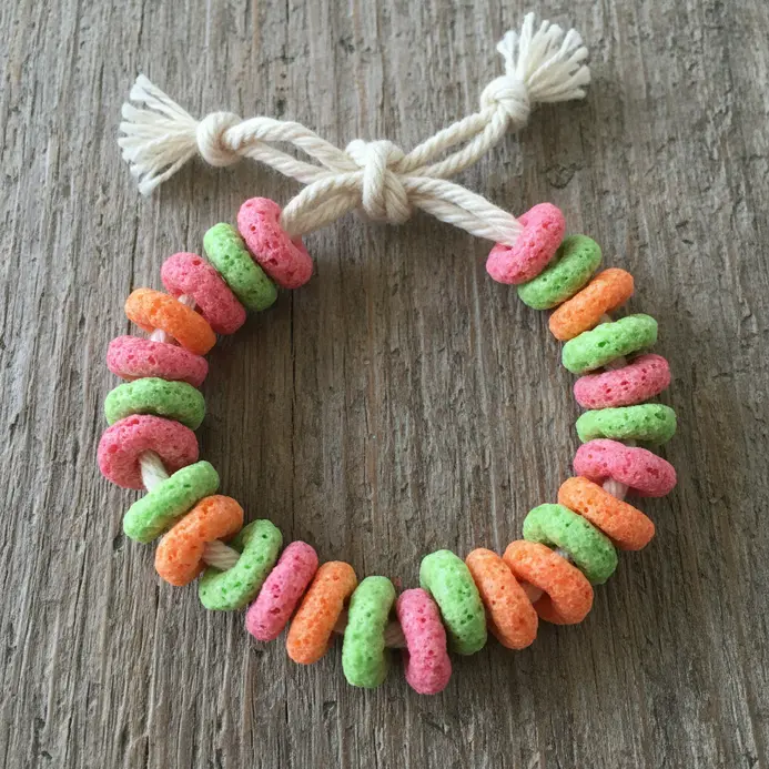 A child's wrist wears a long bracelet strung with exactly 100 pieces of fruit cereal.