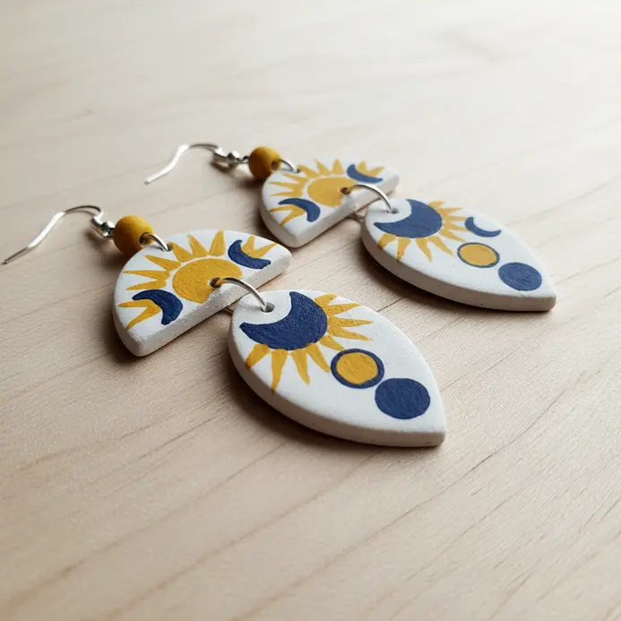 A pair of lightweight earrings with miniature, painted clay charms depicting sun and moon faces.