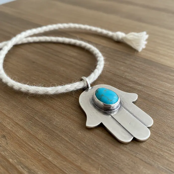 A dainty silver chain holding a pendant in the shape of a Hamsa hand with a tiny blue eye bead.