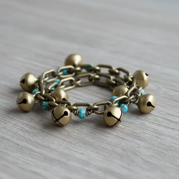 A thin chain bracelet adorned with several miniature brass bell charms and a few colorful beads.