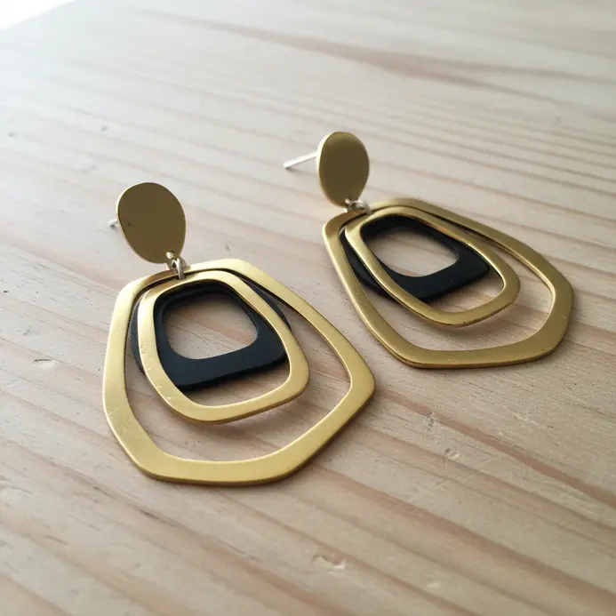 A pair of substantial, circular brass earrings with intricate geometric patterns cut out of the metal.