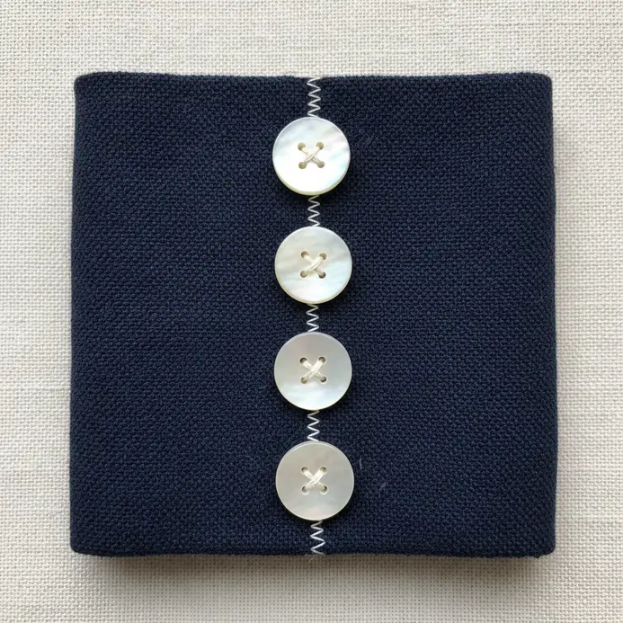 A navy blue fabric cuff bracelet with a precise vertical line of seven identical mother-of-pearl buttons.