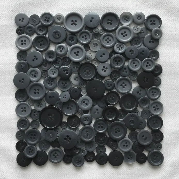 An abstract composition on canvas featuring clusters of grey, black, and white buttons applied in varying depths.