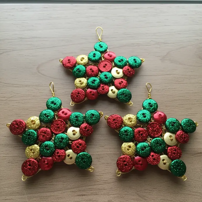 Three star-shaped forms covered in reflective red, green, and gold buttons, with hanging loops at the points.