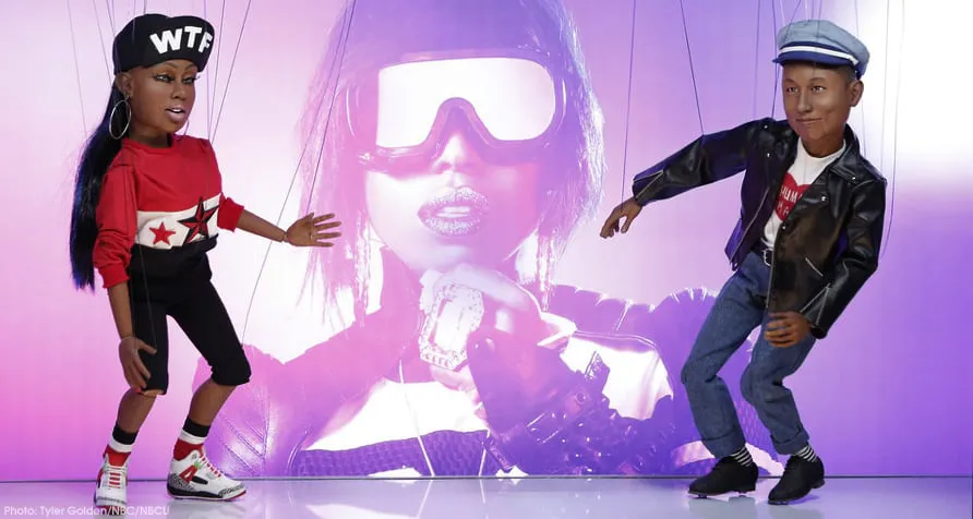Missy Elliott and Pharrell Williams likeness marionette puppets dancing on strings in front of a large projected image of Missy Elliott.