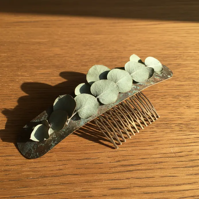A bronze-toned hair comb holding several preserved eucalyptus leaves with a silvery finish.