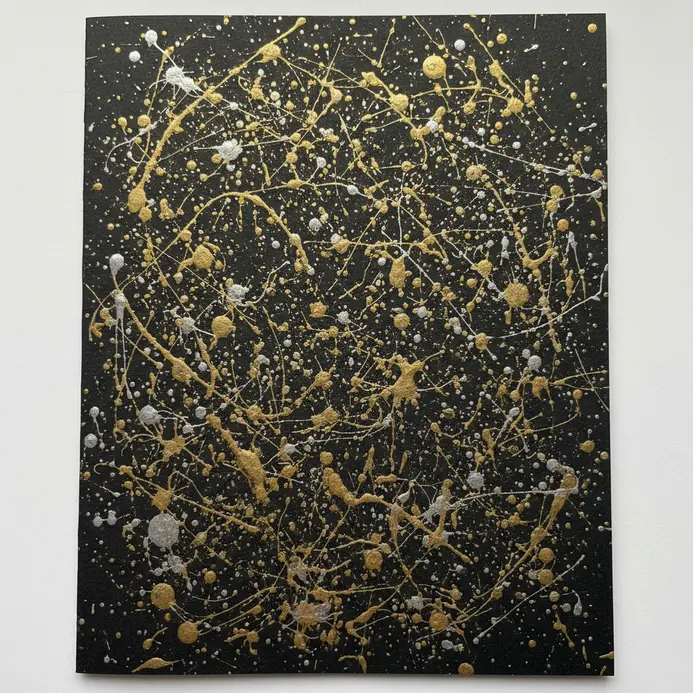 A dark cardstock background covered with energetic splatters and drips of shiny gold and silver metallic ink.