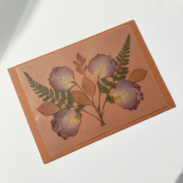 A translucent vellum overlay on a card base with delicate pressed flowers and foliage arranged artfully.