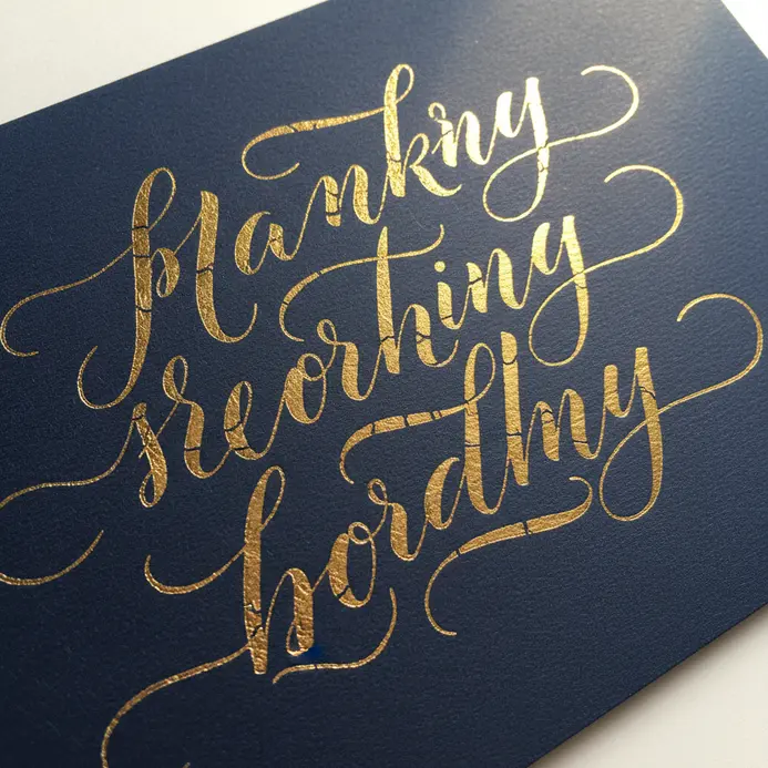 A dark navy card with a single elegant word or phrase written in shiny gold foil calligraphy.
