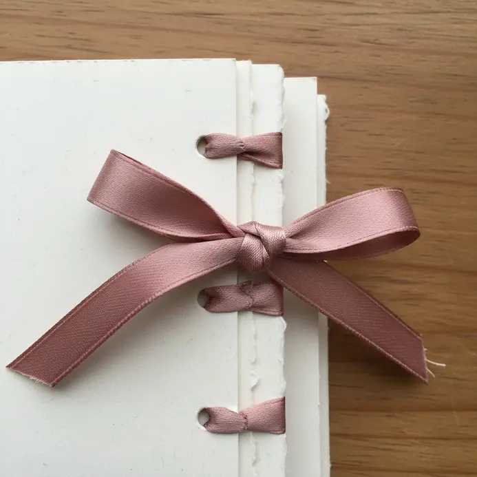 The bound edge of a scrapbook with a satin ribbon tied in a bow around the spine, with tails trailing.