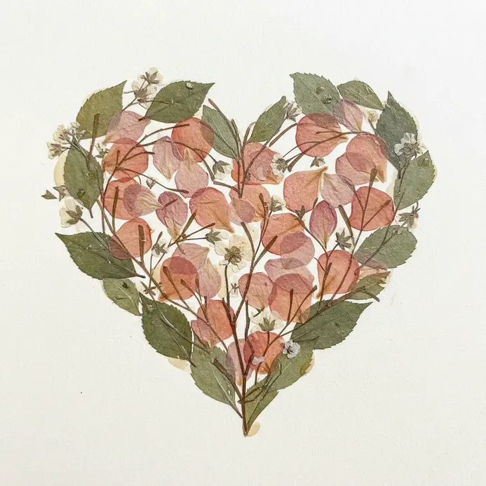 A kraft paper scrapbook page with a heart outline filled with delicate pressed flowers and ferns.