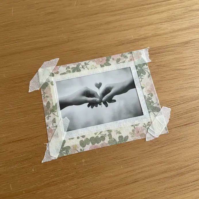 A square photo mounted on paper with strips of floral washi tape creating a bottom border like a Polaroid frame.