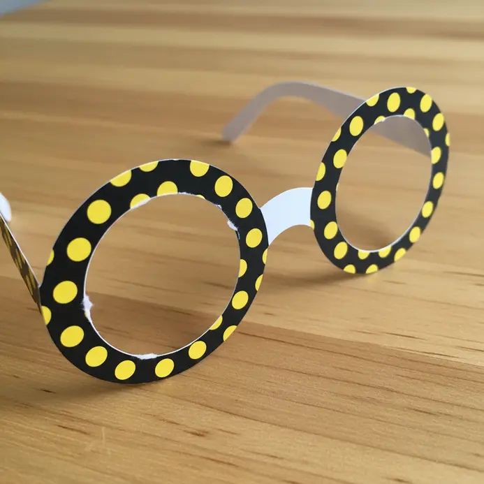 Yellow paper glasses covered with an even pattern of black polka dots.