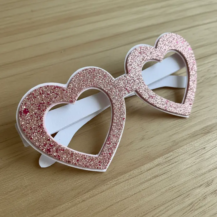 Pink paper glasses where the frames are shaped like two large, glitter-covered hearts.