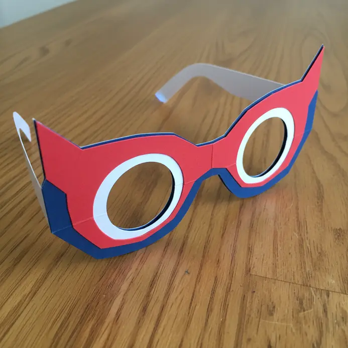 A single paper craft piece forming glasses connected to a bold, angular superhero mask.