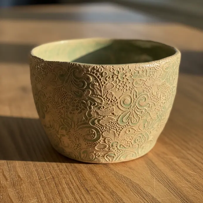 A small pinch pot planter featuring a detailed lace pattern pressed into the clay surface.