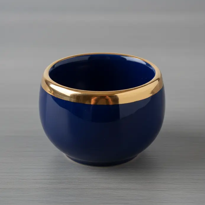 A small, glossy clay pot with a precise band of gold paint around the rim.
