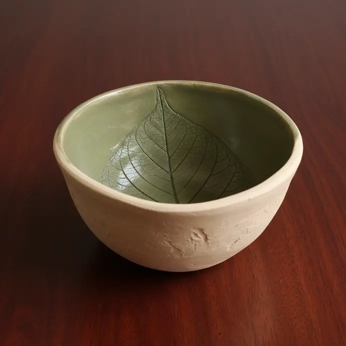 A simple clay bowl decorated with the natural impression of a leaf.