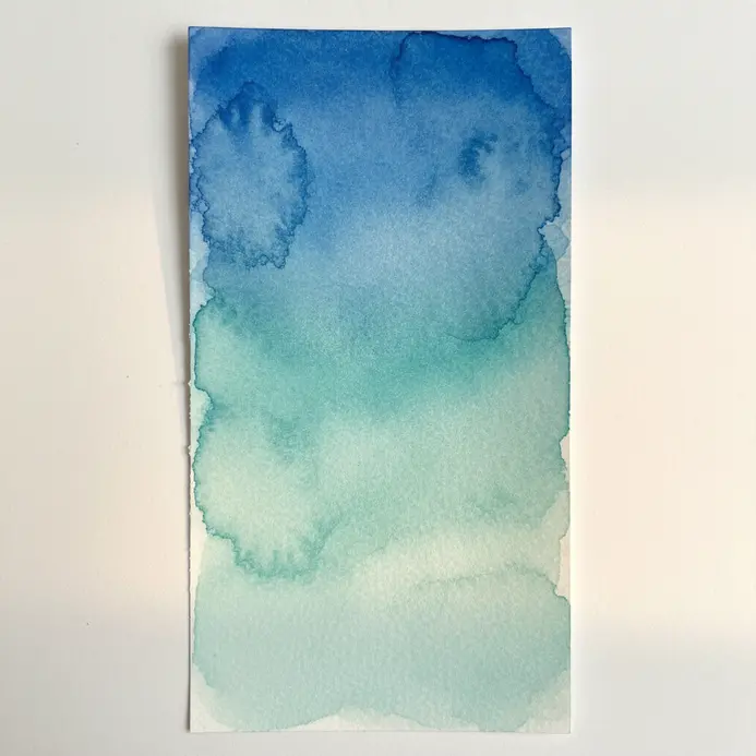 A smooth ombre gradient of blue watercolor washes resembling ocean waves on a paper strip.