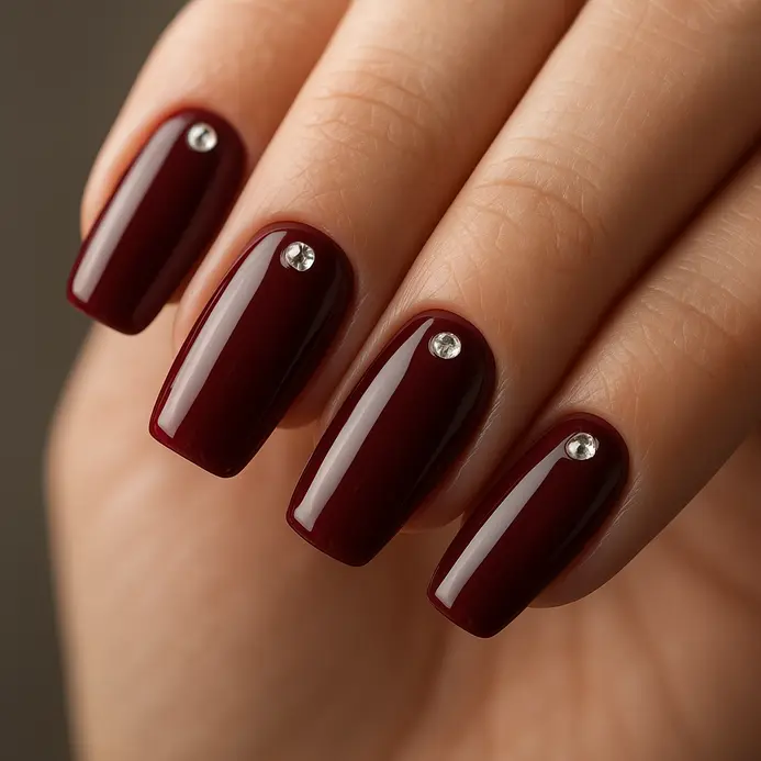A deep red glossy nail with one clear round rhinestone placed off-center.