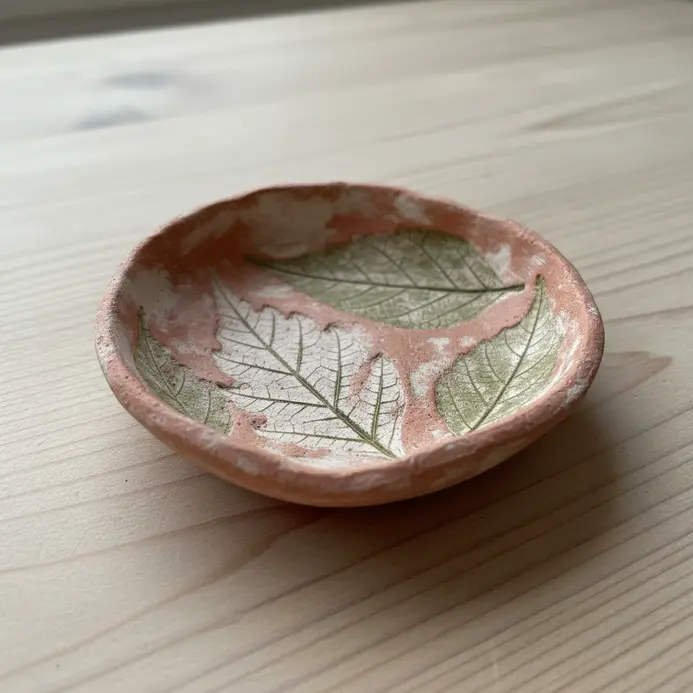 A shallow air dry clay dish with a detailed leaf impression pressed into its surface.
