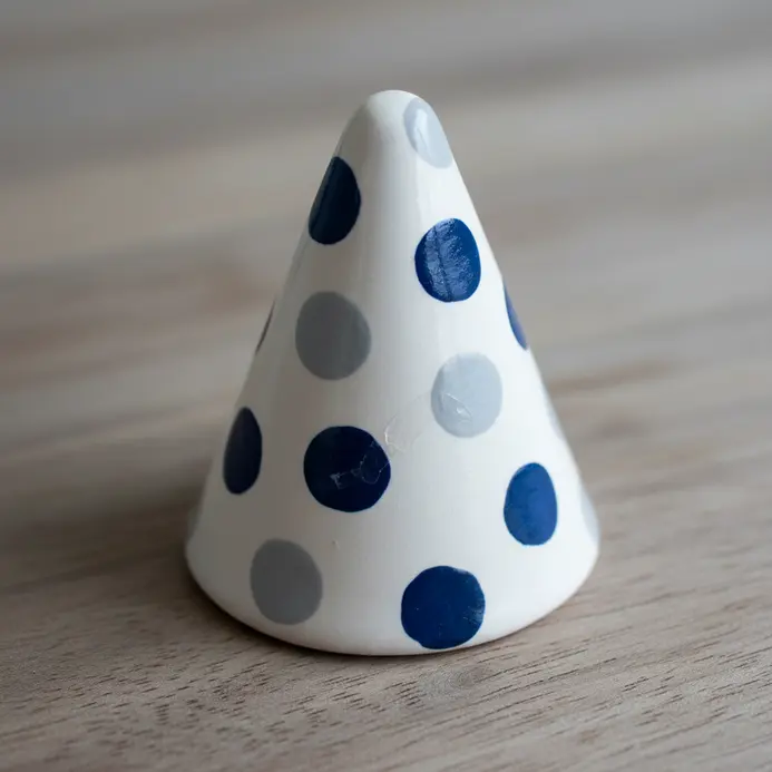 A conical air dry clay ring holder with small, applied clay dots in a contrasting color.