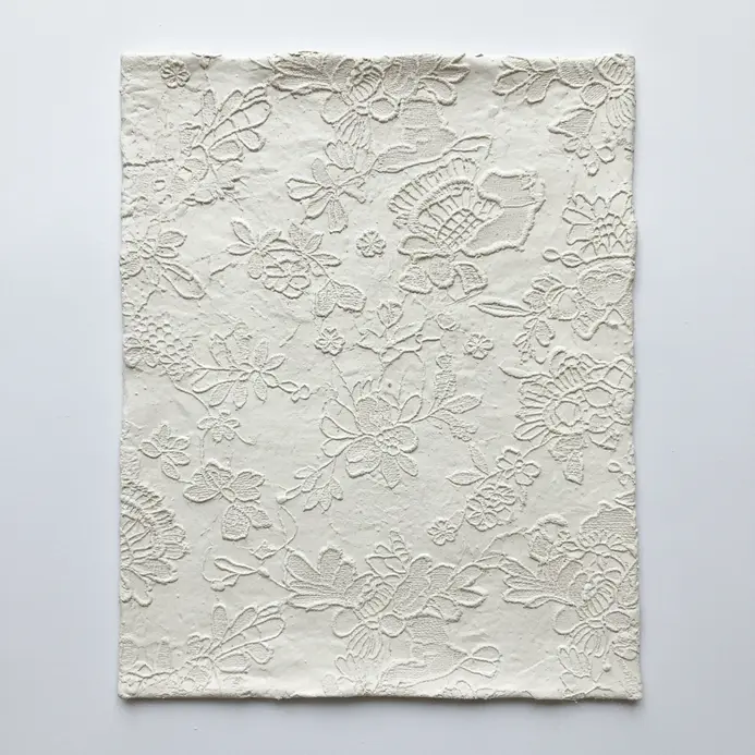 A round slab of air dry clay pressed with lace to create a delicate, textured pattern.