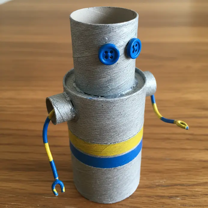 A silver and red paper mache robot with a cylindrical body made from tubes, button eyes, and pipe cleaner arms.