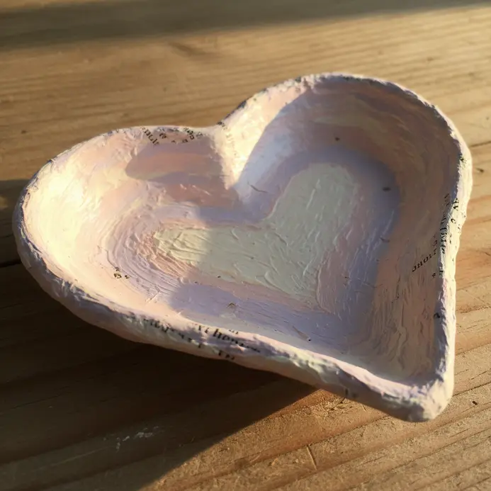 A shallow pink paper mache dish in a heart shape, perfect for holding jewelry, formed over a bowl mold.