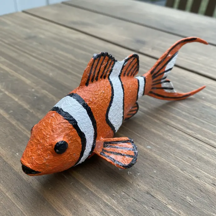 A colorful paper mache clownfish wall decoration with detailed fins and stripes, formed over a balloon shape.