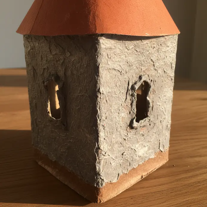 A gray stone-textured paper mache castle turret built onto a square cereal box, complete with paper cone roof and window cutouts.