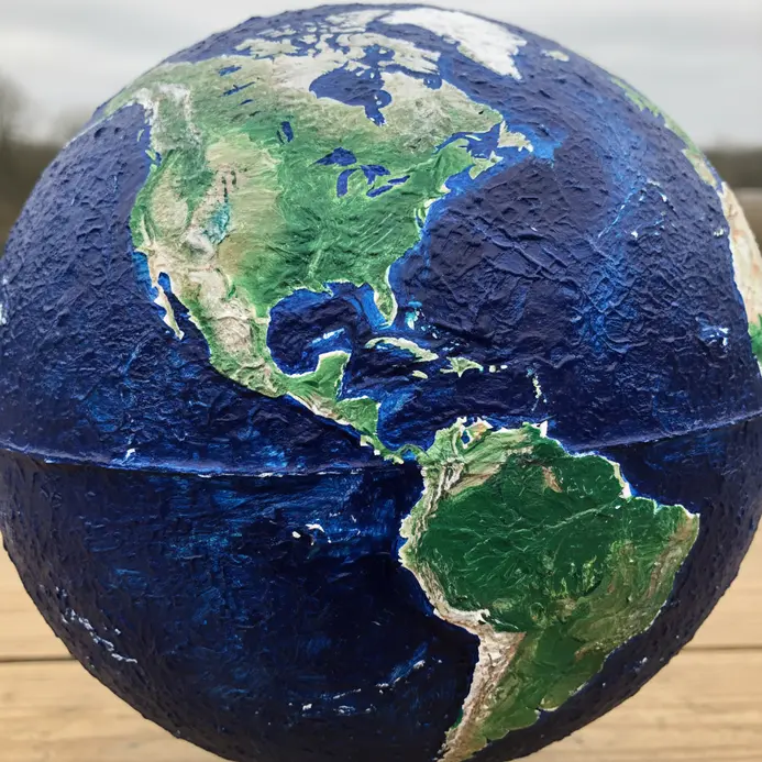 A blue and green paper mache globe depicting continents, formed over a balloon and mounted on a small wooden base.