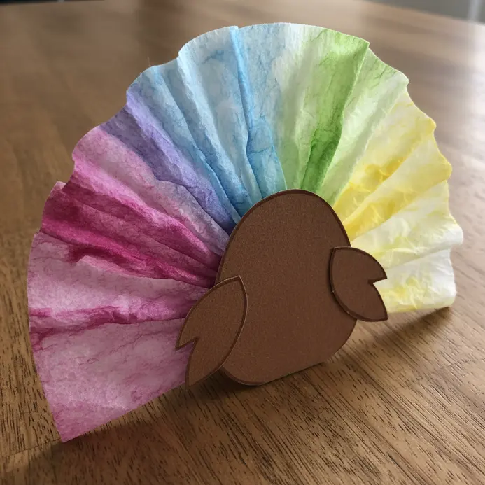 A paper turkey body is attached to a fan of coffee filters dyed with watercolors to create rainbow feathers.