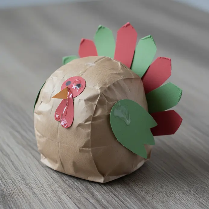 A standard brown paper lunch bag is transformed into a turkey puppet with a paper beak, wattle, and feather decorations.