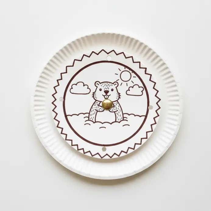 Two paper plates fastened together, one with a window showing a groundhog that appears when the top plate spins.