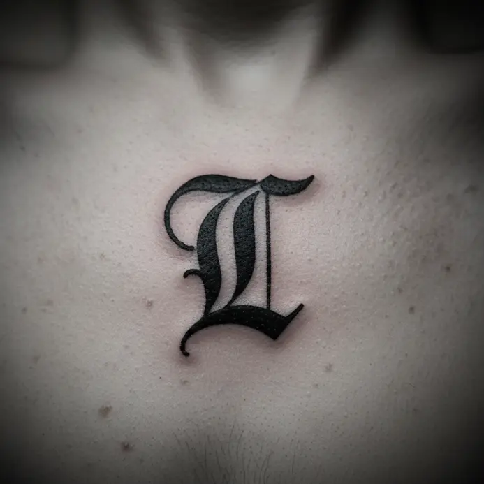 A thick, traditional Gothic-style letter T tattoo in a prominent chest placement.