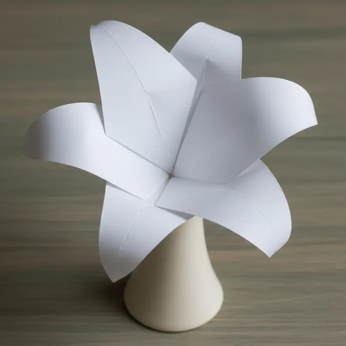 A clean, modern white paper lily with sharp, precise folds and geometric petals on a sleek black stand.