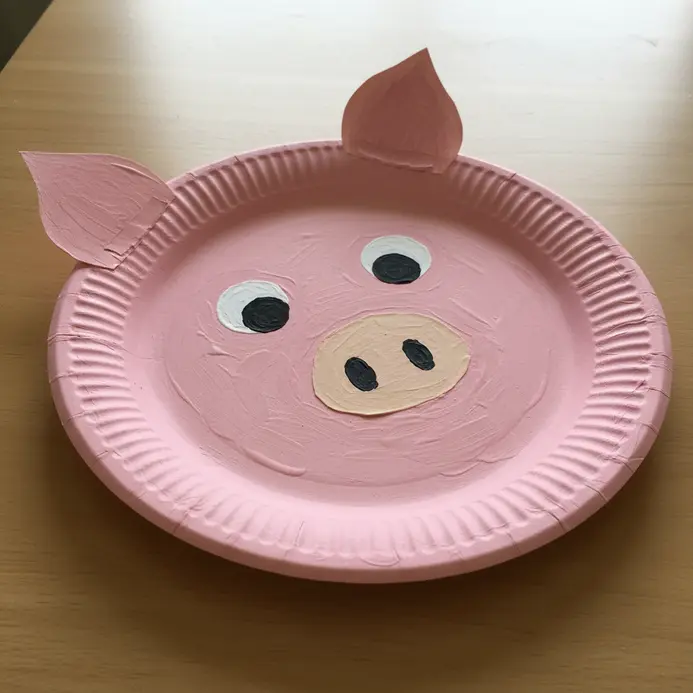 A simple pink paper plate pig face with large floppy ears and a round paper snout.
